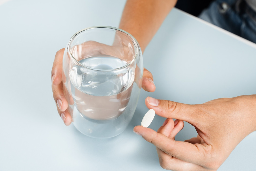 personne qui prend une pilule avec un verre d'eau