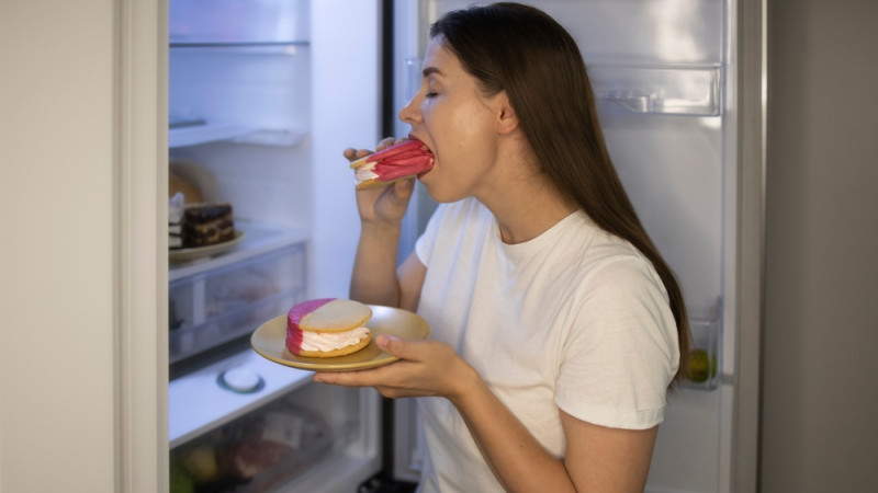 Femme qui mange des gâteaux devant son frigo