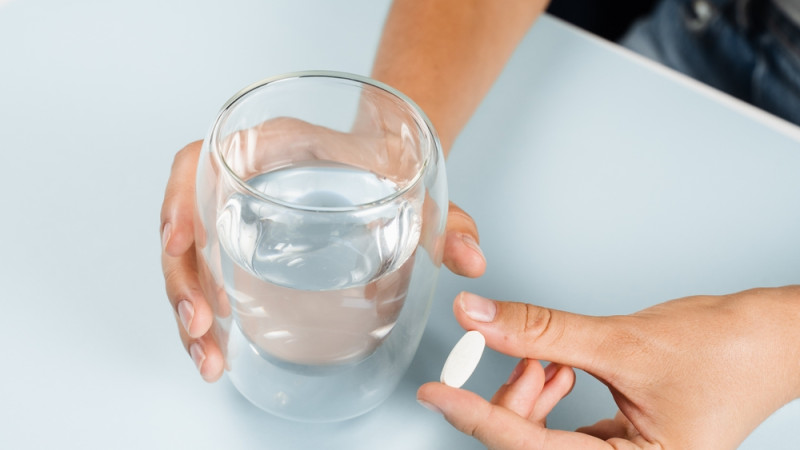 personne qui prend une pilule avec un verre d'eau