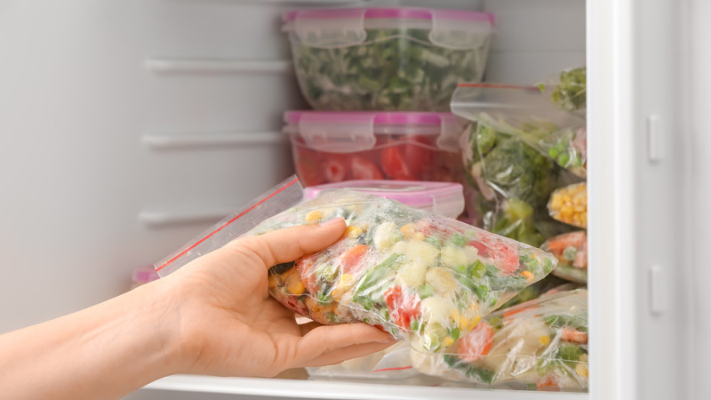 femme place des légumes dans le congélateur 