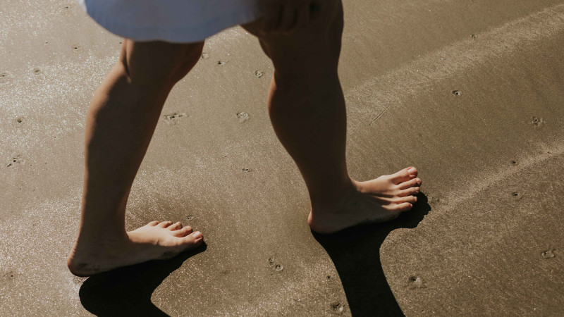 Gros plan sur les pieds nus d'une femme marchant sur une plage ensoleillée, projetant des ombres.