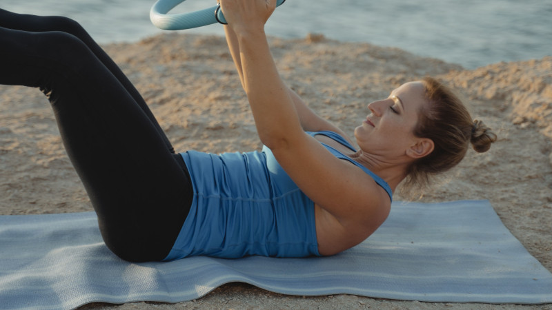 Une femme adulte effectue des exercices de yoga avec un anneau au bord de l'océan.