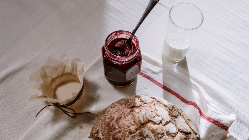 Une scène de petit-déjeuner confortable avec du pain rustique, un pot de confiture et un verre de lait sur une nappe texturée.