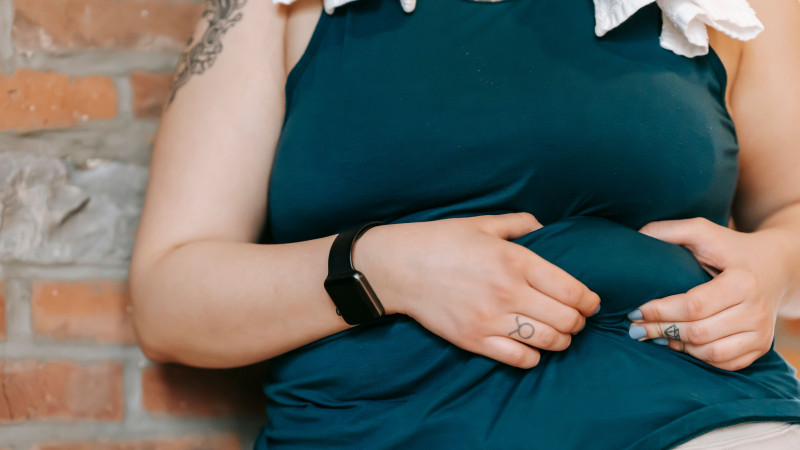 Femme en débardeur turquoise tenant son ventre, mettant en avant la positivité corporelle et la prise de conscience du poids.