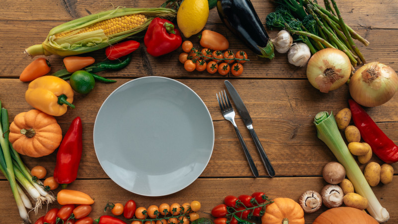 Une variété vibrante de légumes frais sur une table en bois entourant une assiette vide.