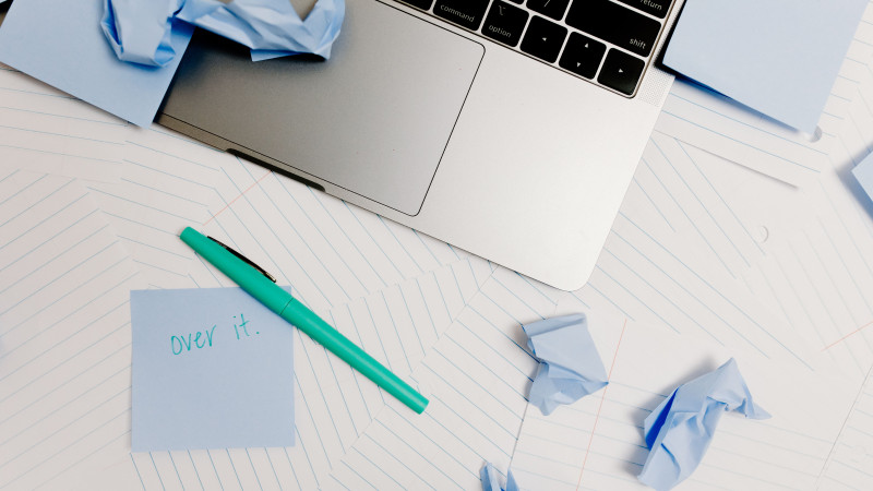 Un bureau en désordre avec un ordinateur portable, un post-it disant 'j'en ai marre', et des notes froissées symbolisant l'épuisement.