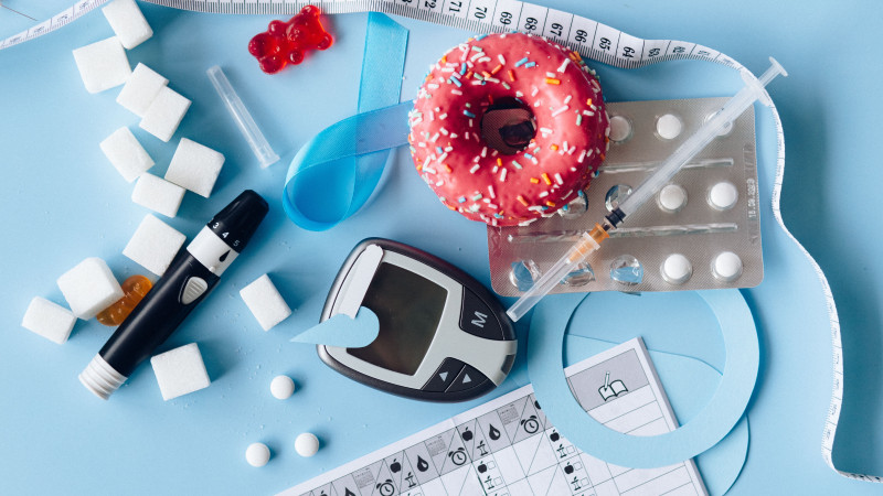 Image de nature morte d'équipement de gestion du diabète, de sucreries et de médicaments disposés artistiquement sur un fond bleu.