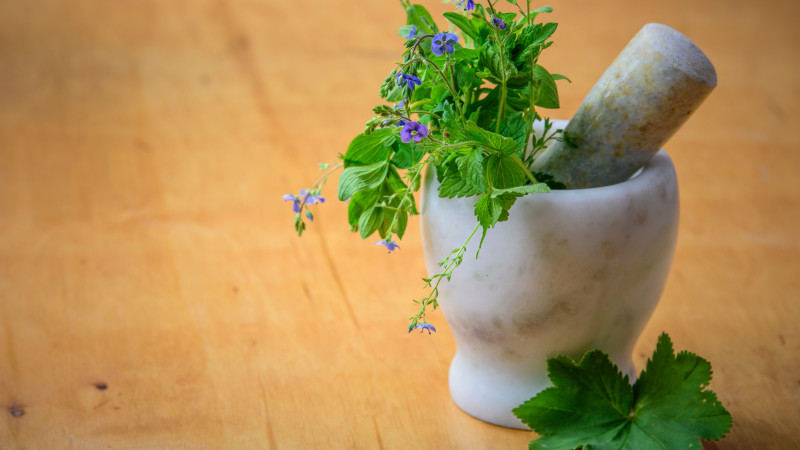 Mortier et pilon en marbre avec des herbes et des fleurs fraîches sur une table en bois, améliorant l'esthétique de la santé naturelle et de la cuisine.