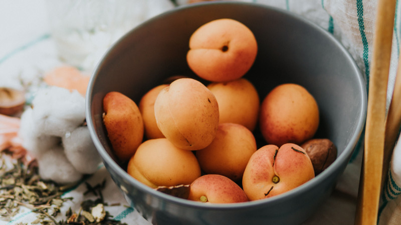 Gros plan sur des abricots frais dans un bol gris, posé sur une table de cuisine et entouré d'herbes aromatiques.