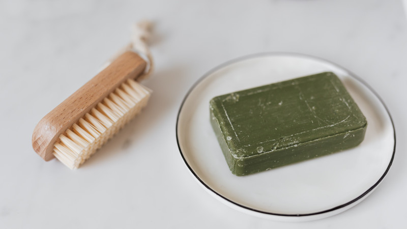 Photo minimaliste d'un savon organique vert et d'une brosse en bois sur marbre pour un soin naturel.