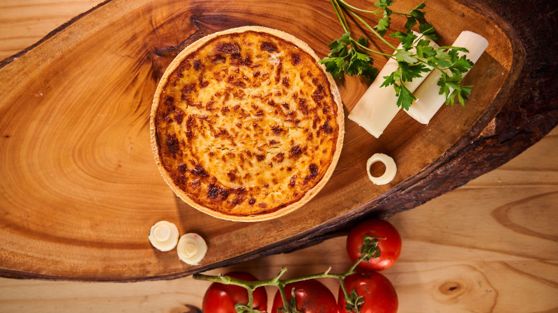 Quiche au fromage alléchante sur planche de bois avec garniture de tomates et de persil, parfaite pour les thèmes culinaires.