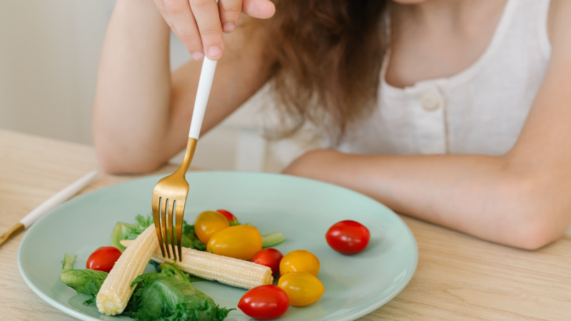 Une jeune fille en robe blanche savoure une salade saine avec des légumes frais dans une assiette.