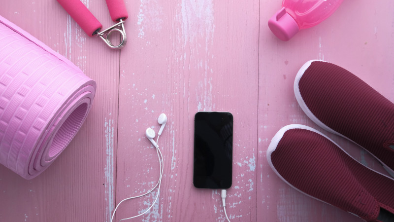 Vue de dessus des accessoires de fitness, y compris un tapis de yoga, des chaussures, une bouteille d'eau et un smartphone sur du bois rose.