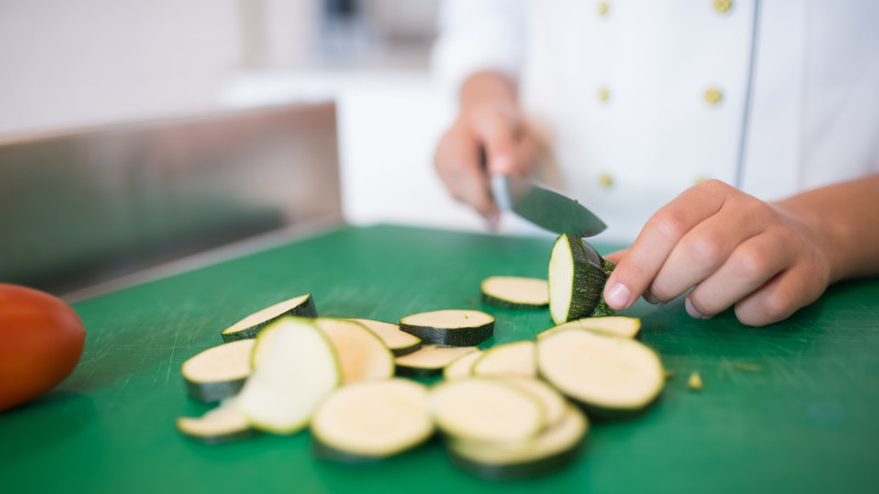Gros plan d'un chef tranchant des courgettes sur une planche à découper verte pour une cuisine fraîche.