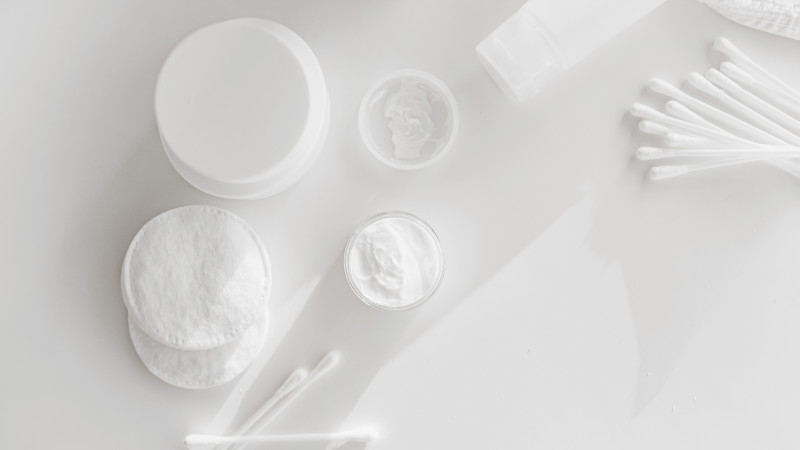 Disposition à plat des essentiels de soins de la peau avec des tampons en coton et des cotons-tiges sur un fond blanc.