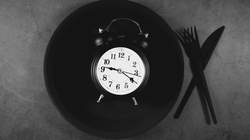Alarm clock on black plate with cutlery on grey background