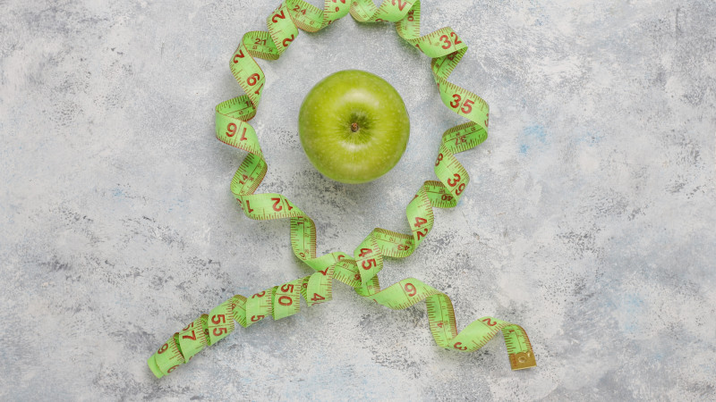Pomme verte fraîche, ruban à mesurer et bouteille d'eau fraîche sur béton gris