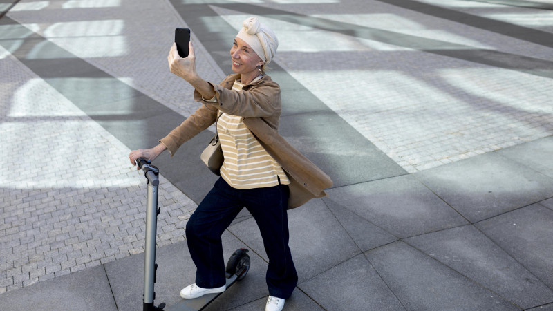 Femme âgée avec un scooter électrique dans la ville prenant un selfie