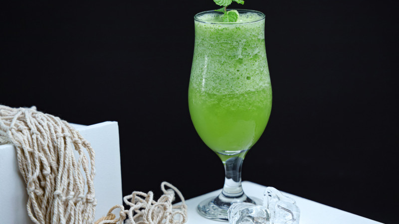 Un smoothie vert frais et sain dans un verre avec une garniture de menthe, sur fond sombre.