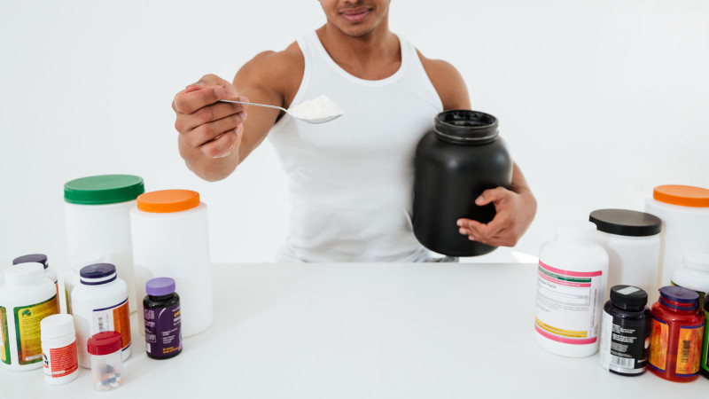 Un sportif debout sur un mur blanc tenant des vitamines