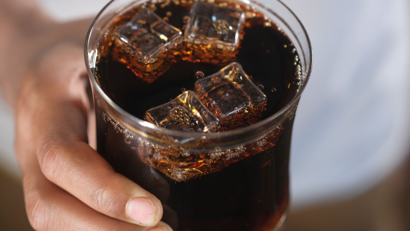 Gros plan sur une main tenant un verre de soda noir avec des glaçons, créant une sensation rafraîchissante.