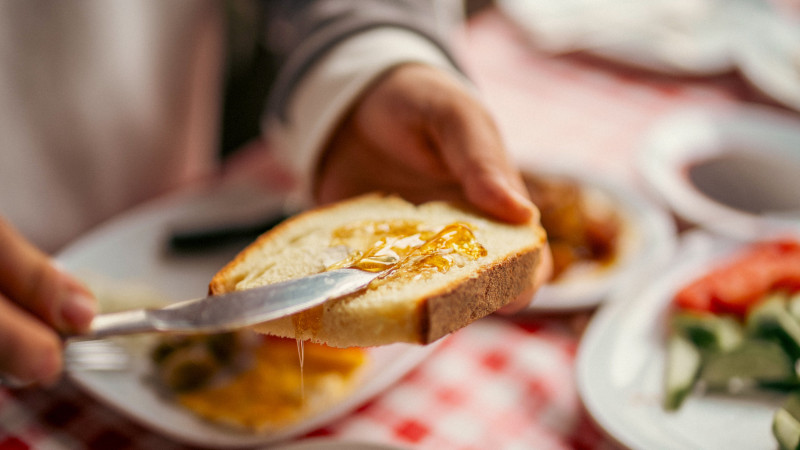 Une délicieuse scène de petit-déjeuner avec du miel tartiné sur du pain, sublimant le repas matinal.