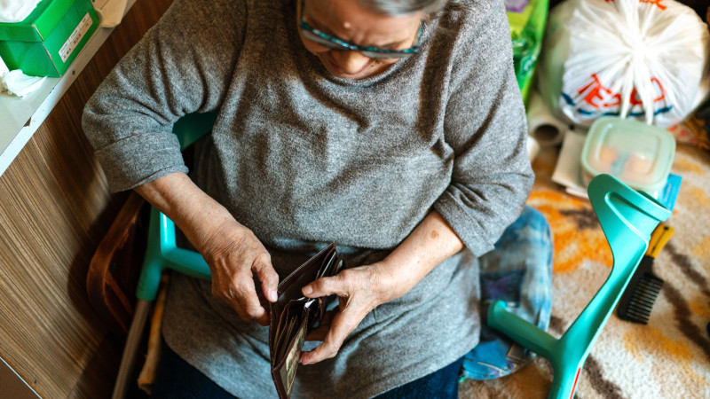 Femme âgée assise à l'intérieur gérant son portefeuille. Thème de soins à domicile.
