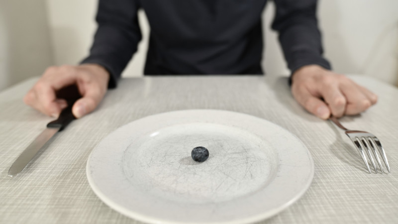 Une seule myrtille sur une assiette rayée symbolise un régime minimaliste et le contrôle des portions.