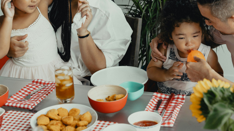 A family eating chicken nuggets and watermelon at a table in a home