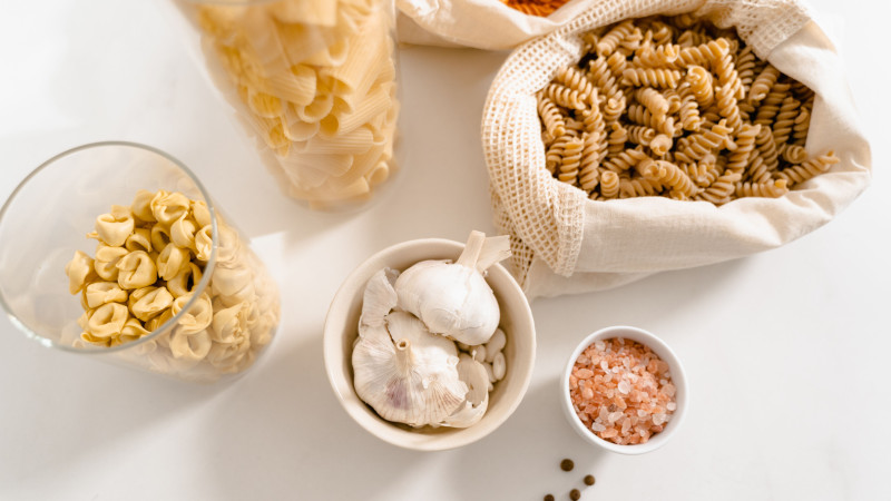 Vue de dessus des ingrédients de pâtes biologiques et des assaisonnements, avec de l'ail, du sel rose et des sacs réutilisables.