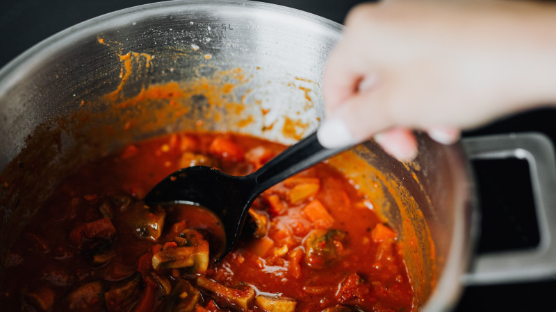 Ragoût de légumes fraîchement cuisiné avec des tomates et des épices dans une casserole, mélangé à la main.