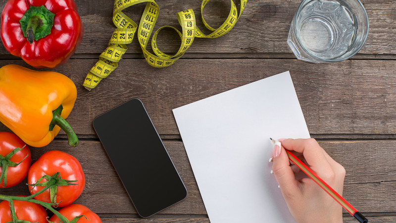 Régime alimentaire conceptuel, plan amincissant avec vue de dessus de légumes maquette. Une main féminine dans un bracelet de sport écrit un article sur une bonne nutrition