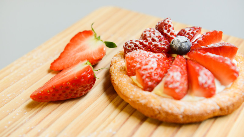 Une délicieuse tarte aux fraises avec de la crème fraîche et du sucre glace servie sur une planche en bois.