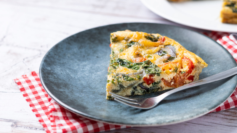 Frittata italienne faite avec des épinards, des tomates, des oignons et des poivrons sur une table en bois blanc