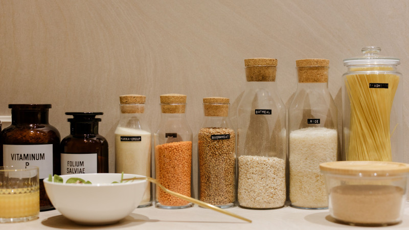 Une variété de grains et de pâtes dans des bouteilles en verre étiquetées, exposées sur un comptoir de cuisine.