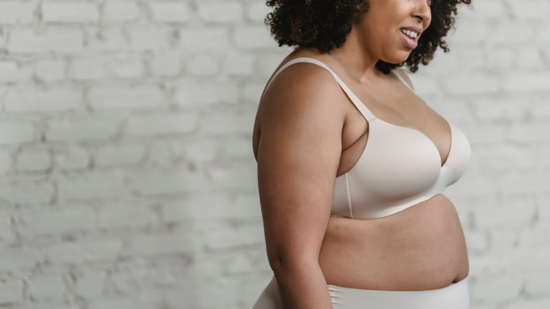Une femme grande taille joyeuse en lingerie se tenant contre un mur en briques, embrassant la positivité corporelle.