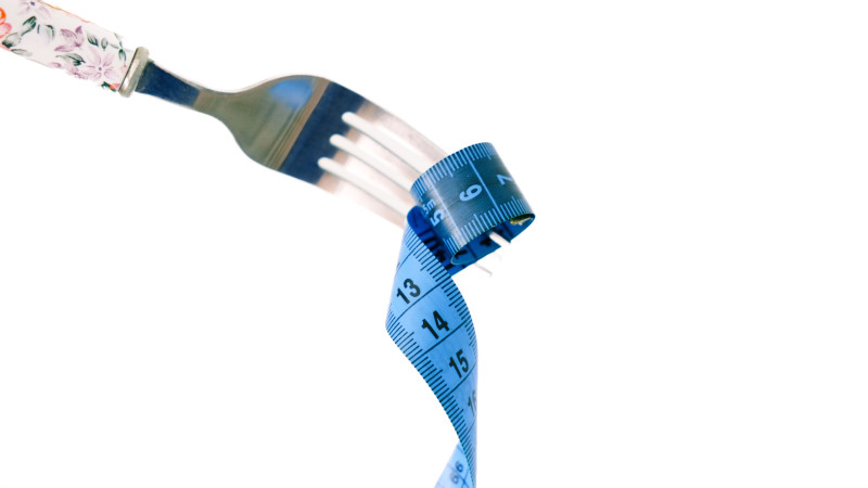 Une fourchette enroule un mètre ruban bleu, symbolisant la gestion du poids et la santé.