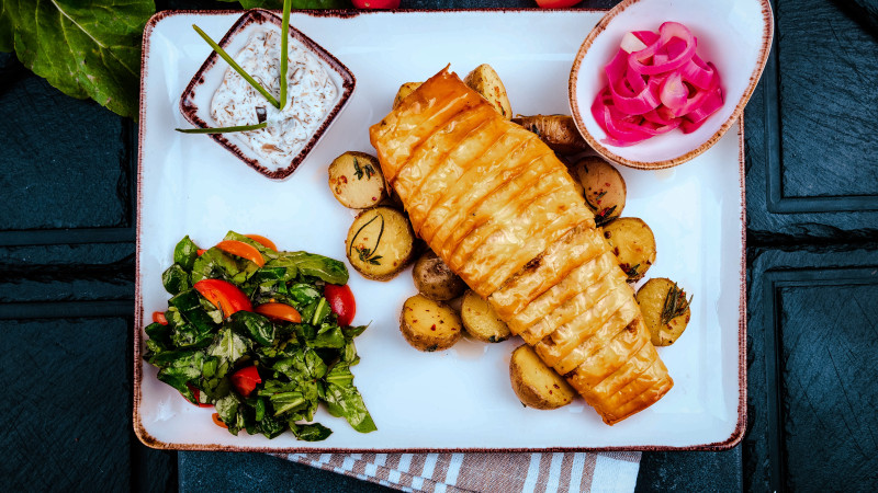 Délicieux poisson rôti avec des pommes de terre et des légumes frais servi sur un plateau blanc.