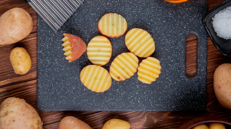 Vue de dessus de tranches de pommes de terre ébouriffées sur une planche à découper avec du beurre à l'ail et du sel sur une surface en bois