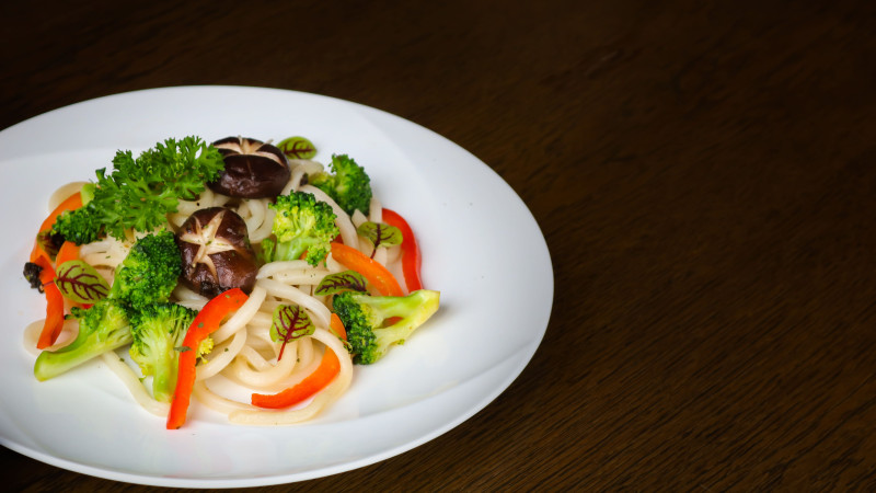 Une assiette colorée de nouilles udon aux légumes et aux champignons shiitake, idéale pour un repas sain.