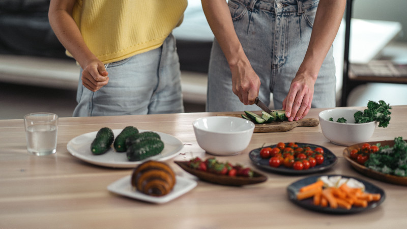 Deux personnes préparant un repas végétarien sain avec des légumes frais et des collations sur une table en bois.