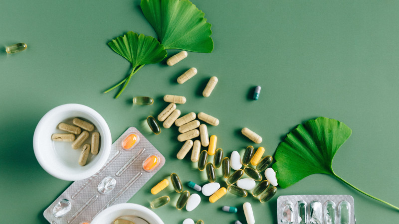 Plongée de divers suppléments et médicaments avec des feuilles de ginkgo sur une surface verte, mettant en avant un concept de remède naturel.