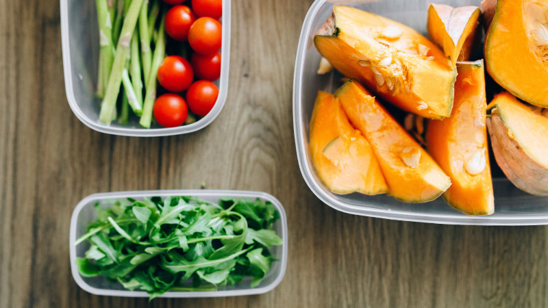 Vue de dessus d'ingrédients frais comprenant de la roquette, des tomates cerises et des courges dans des contenants en plastique sur un fond en bois.