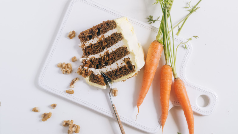 Une tranche de gâteau aux carottes gourmande avec glaçage, noix et carottes fraîches sur une planche à découper.
