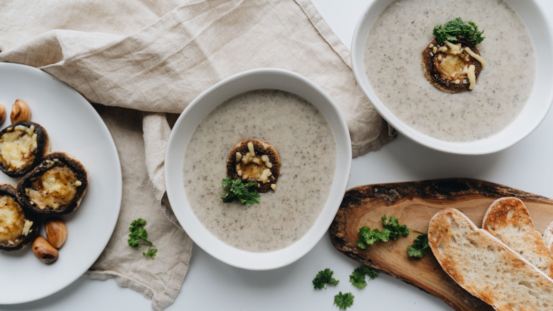 Une vue en plongée de soupe aux champignons, de champignons farcis et de pain sur une planche en bois.